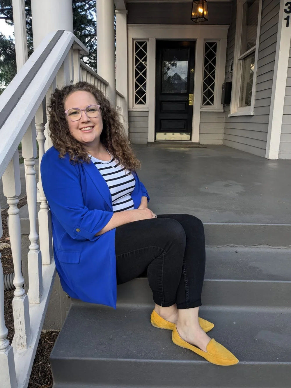 Katie in a blue blazer on the steps of a house, smiling